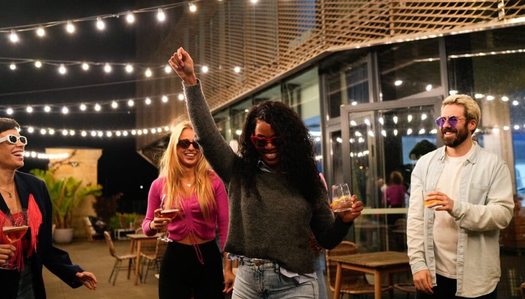 Multiethnic friends enjoying drinks and dancing at rooftop party