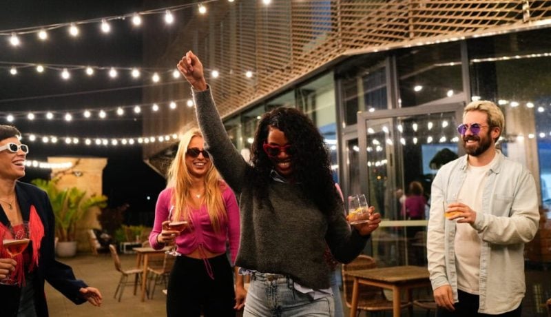 Multiethnic friends enjoying drinks and dancing at rooftop party