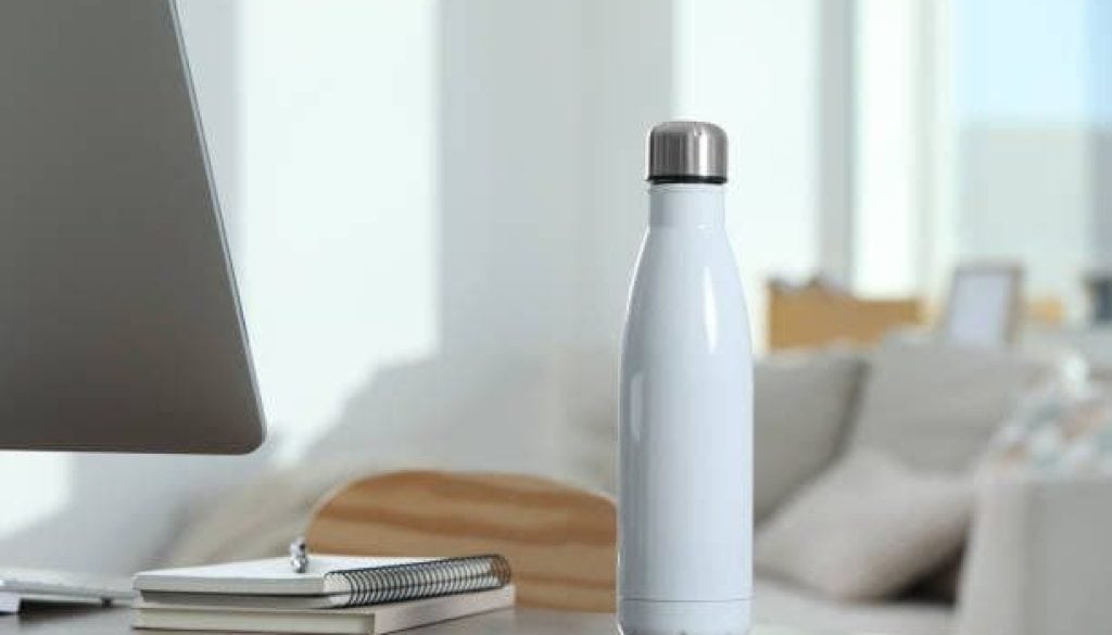 Stylish thermo bottle on wooden table at workplace in office