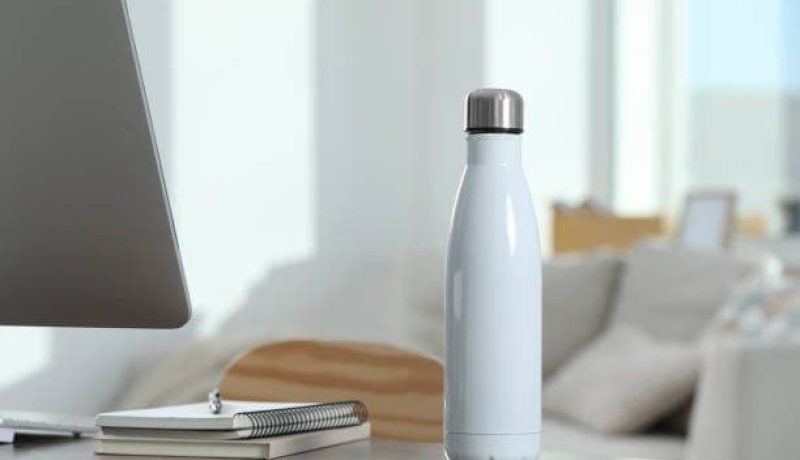 Stylish thermo bottle on wooden table at workplace in office