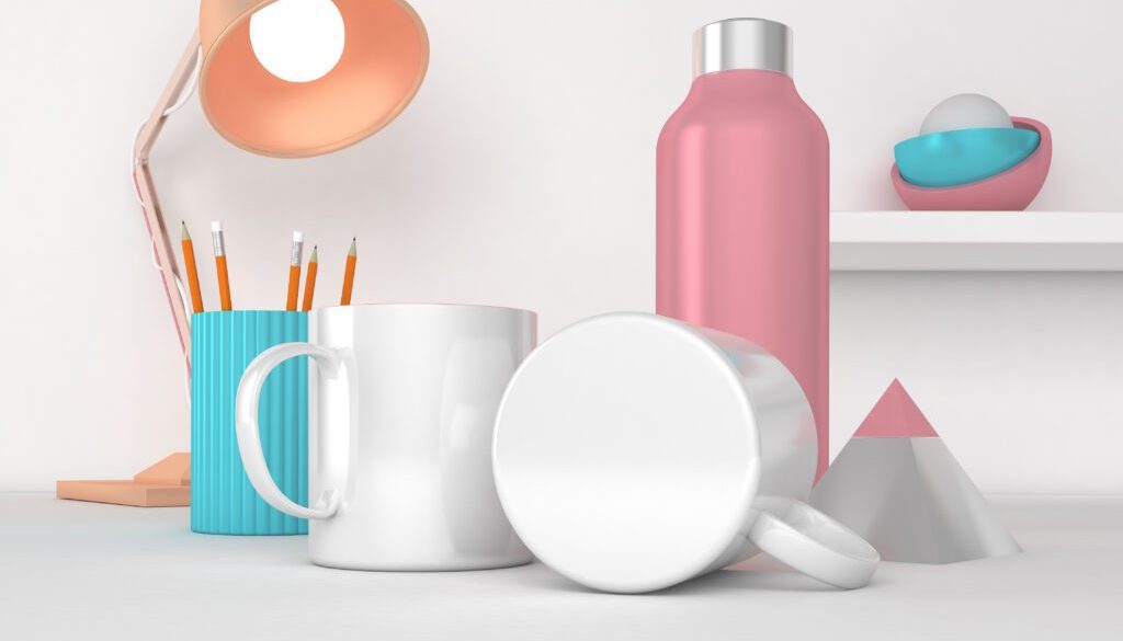 Pink water bottle, white mug, and stationery on a desk with a lamp and decorative objects.