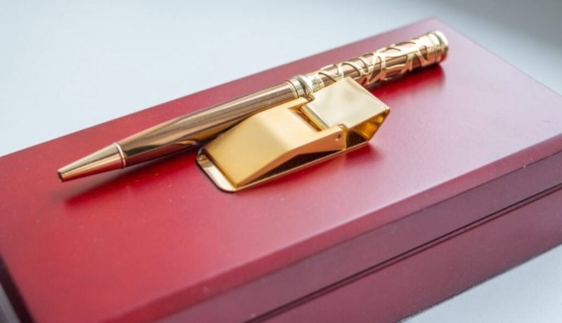 Elegant gold pen and matching gold clip on a red gift box.