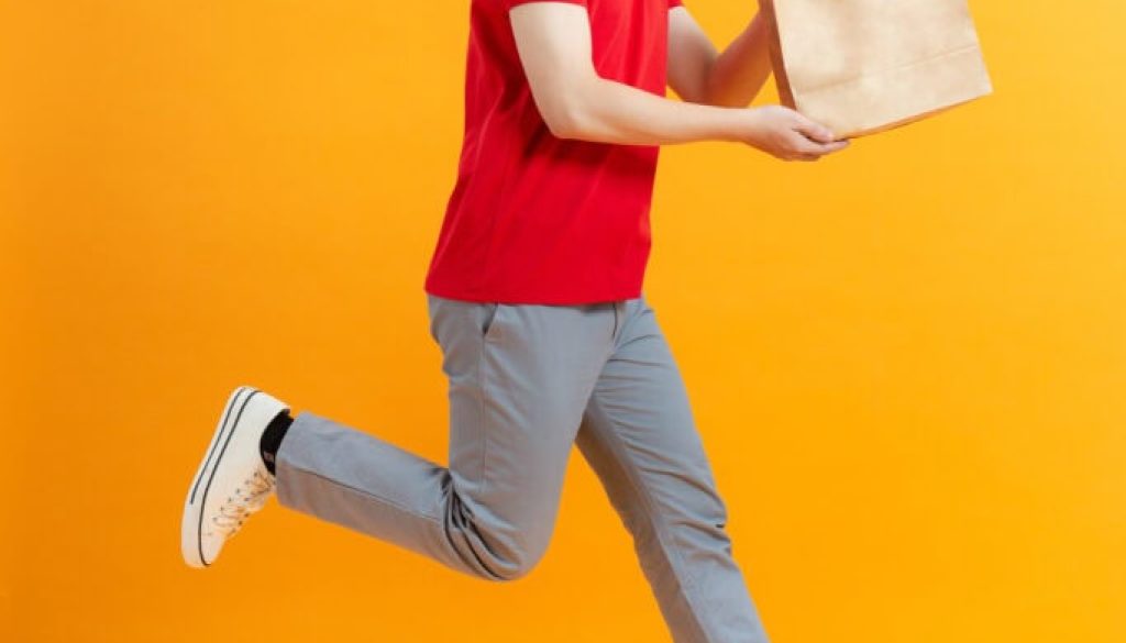 Fun jumping delivery man in red cap t-shirt uniform sterile face mask gloves isolated on yellow background