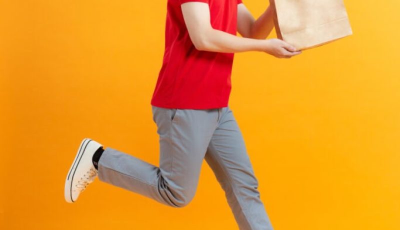 Fun jumping delivery man in red cap t-shirt uniform sterile face mask gloves isolated on yellow background
