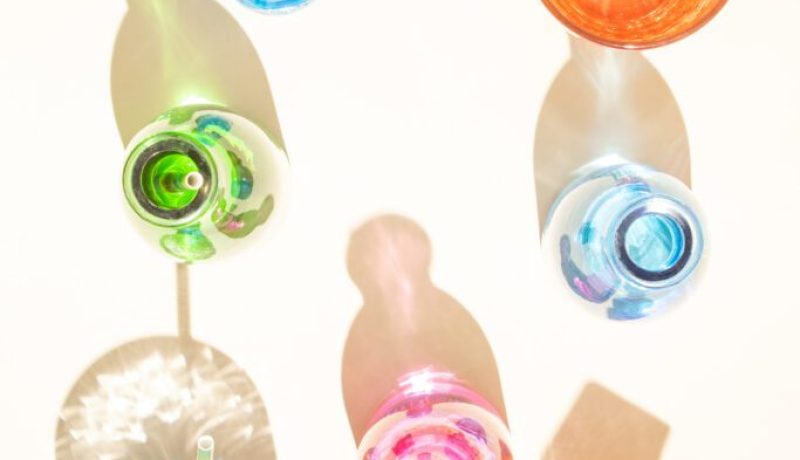 Colorful bottles with cold drinks on sandy background Shadows with shiny colorized reflections Aesthetic abstract design idea Sunny beach day concept