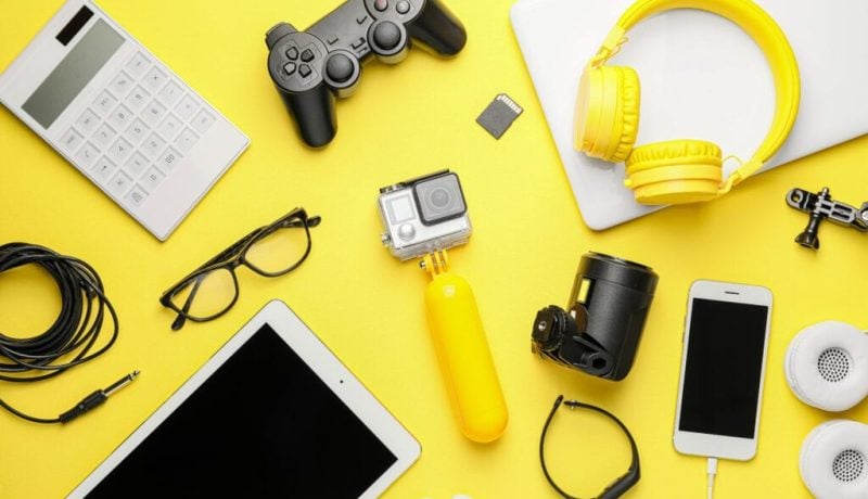 Collection of electronic gadgets and accessories on yellow background.