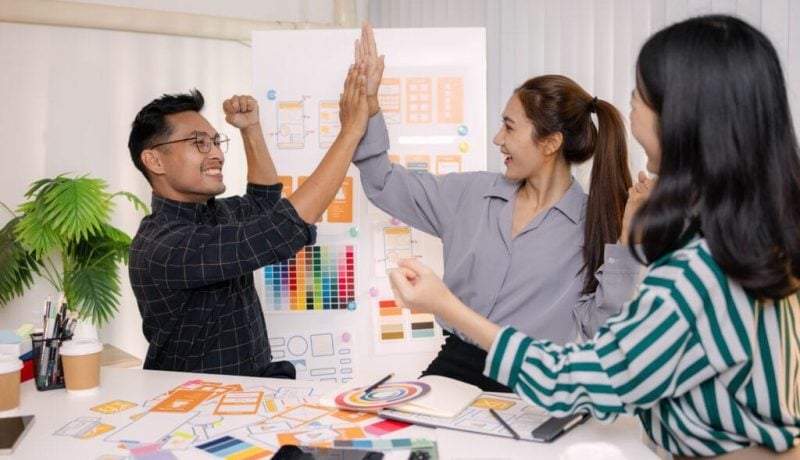 Team celebrating success with high-fives in a creative office environment.