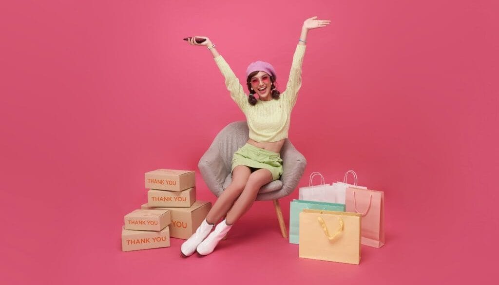 Happy woman with shopping bags and thank you boxes on pink background.