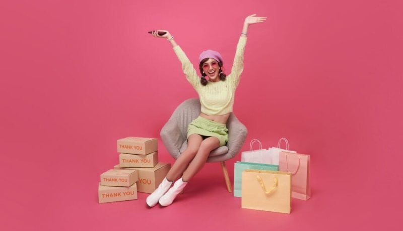 Happy woman with shopping bags and thank you boxes on pink background.