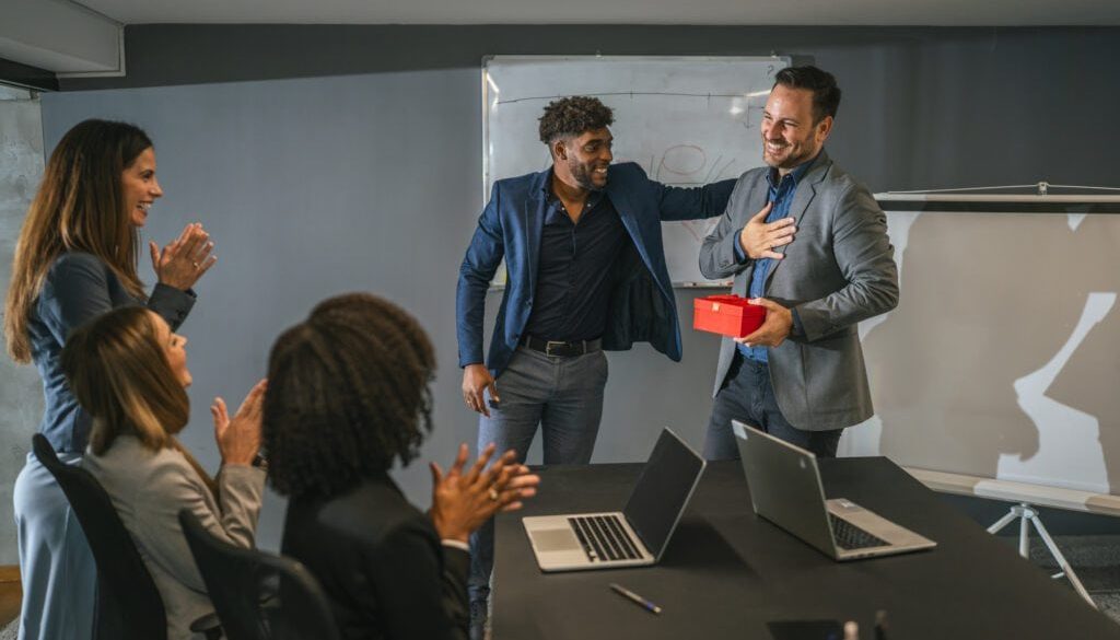 Office colleagues celebrating employee receiving gift at meeting