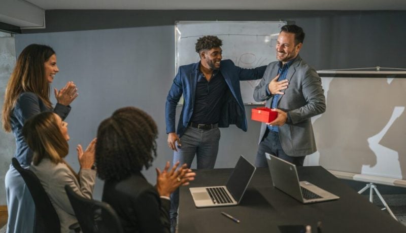 Office colleagues celebrating employee receiving gift at meeting
