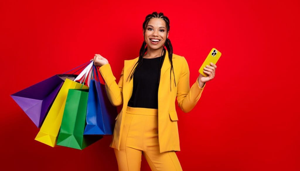 Young woman holding vibrant shopping bags and a phone against red background showcasing stylish and cheerful fashion