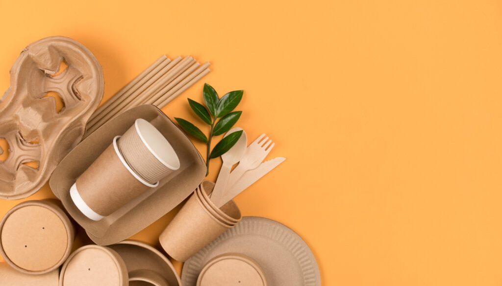 Kraft paper food utensils paper containers and cups drinking straws on orange background with copy space Street food paper packaging concept Top view