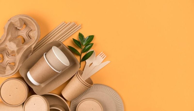 Kraft paper food utensils paper containers and cups drinking straws on orange background with copy space Street food paper packaging concept Top view